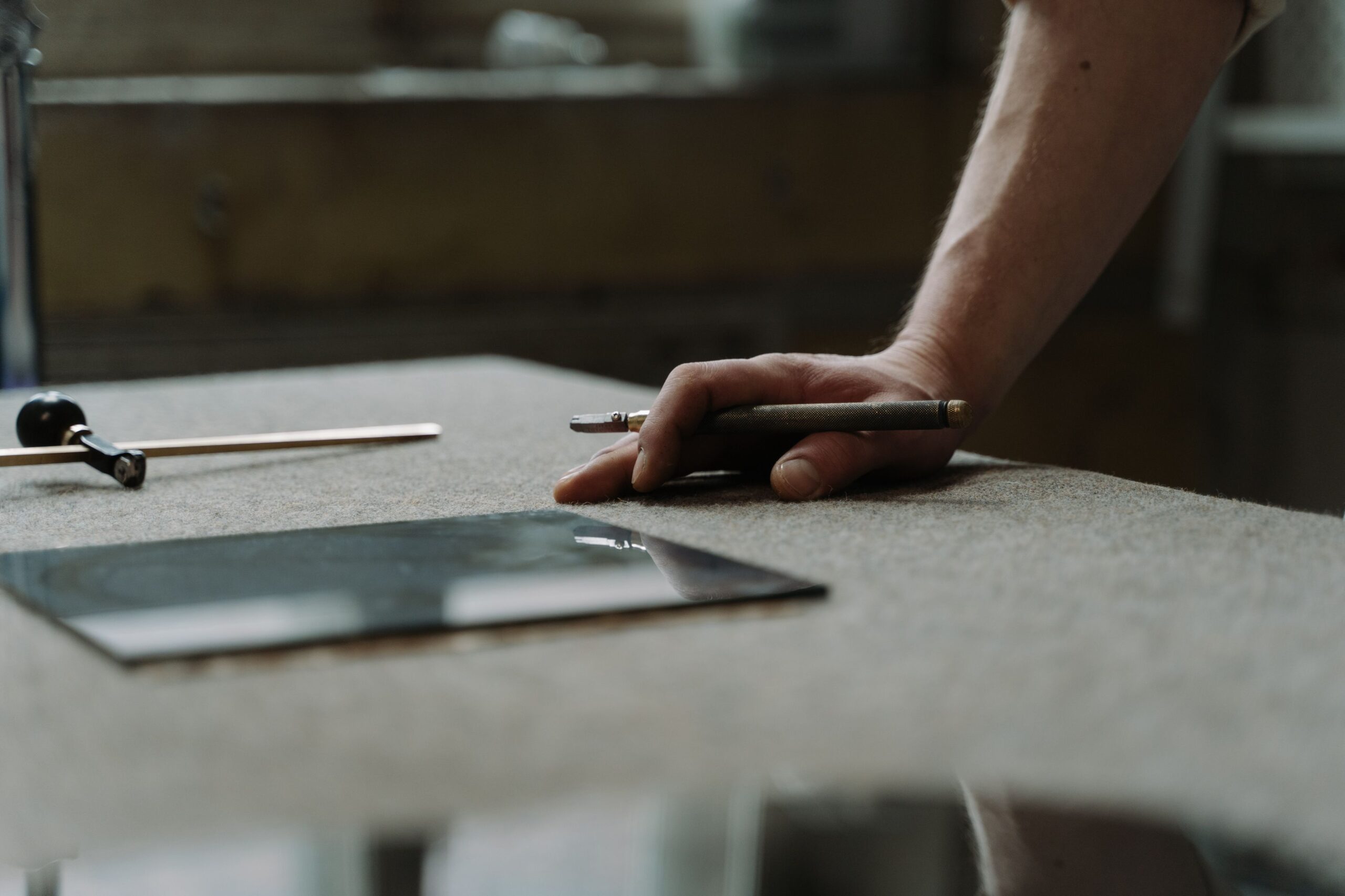 Hand of a craftsman working with a glass cutter in a professional workshop setting.